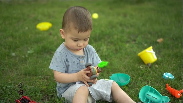 A one-year-old child sits on the grass and plays with toys. Little boy in the park. 4k