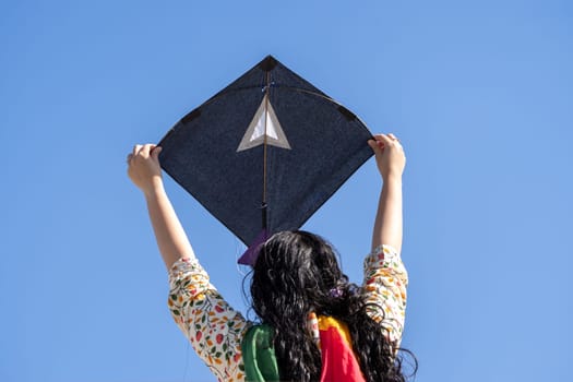 Young girl in traditional indian clothing holding black kite high above head launching it on sankranti republic independence day celebrations