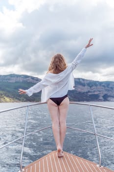 Woman on a yacht. Happy model in a swimsuit posing on a yacht against a blue sky with clouds and mountains.