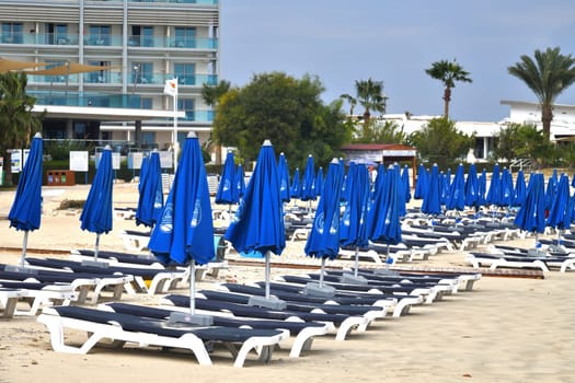 Ayia Napa, Cyprus - November 4. 2018. Empty sun loungers and a folded umbrellas on Makronissos Beach Resort. Swimming season ends