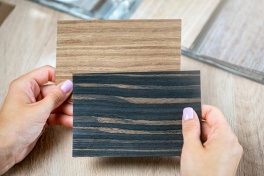 A woman is holding samples of different colors in her hands at the same time and choosing pieces of colored wood to choose a floor. High quality photo