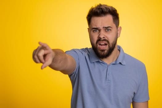 Get out of here. You are fired. Young irritated caucasian man pointing finger away asking to leave him alone, strict boss firing, conflict. Handsome guy isolated on studio yellow background indoors