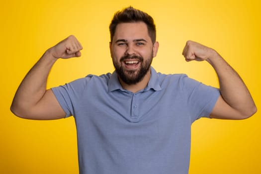 I am strong. Fit sporty caucasian man showing biceps and looking confident, feeling power strength to fight for rights, energy to gain success win. Guy isolated on studio yellow background indoors