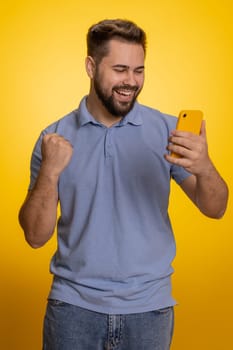 Happy excited amazed joyful caucasian man in t-shirt use smartphone typing browsing shouting say wow yes found out great big win, good news, lottery goal achievemen, celebrating success, winning game
