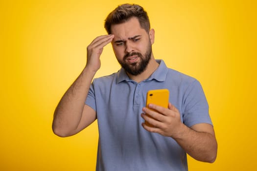 Caucasian man use mobile cell phone typing browsing, loses becoming surprised sudden lottery results, bad fortune, loss, fail. Handsome one guy isolated alone on yellow studio wall background, indoors