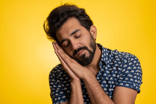 Tired overworked young indian man yawning, sleepy inattentive feeling somnolent lazy bored gaping suffering from lack of sleep. Handsome exhausted hindu guy isolated on studio yellow background indoor