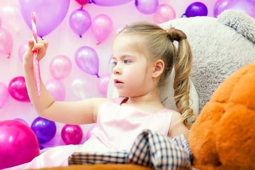 Image of funny little girl attentively looks on lollipop