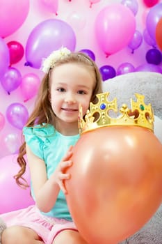 Image of cheerful girl playfully put crown on balloon