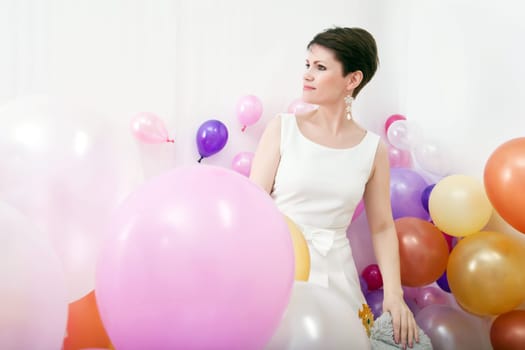 Elegant middle-aged woman posing among colorful balloons