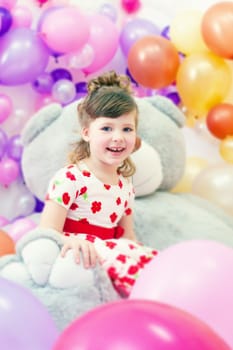 Image of merry little girl posing in playroom with big teddy bear