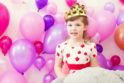 Cute little girl posing in crown on balloons background