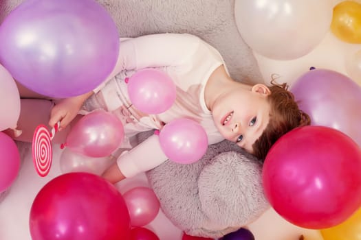 Top view of charming little lady posing with lollipop and balloons