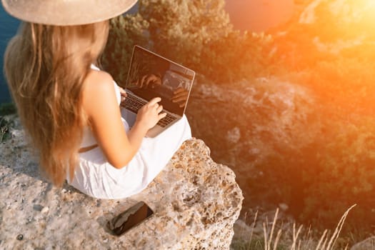 Freelance happy woman typing on her laptop, enjoying the picturesque sea view, highlighting the idea of working remotely with a relaxed and pleasant atmosphere