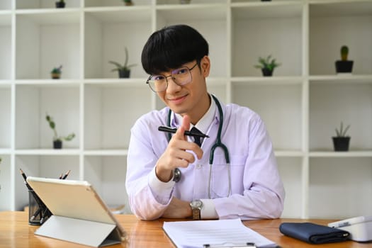 Portrait of general practitioner doctor in white uniform sitting in modern workplace and smiling to camera.