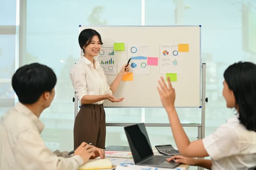 Confident female employee pointing at whiteboard, presenting sales report, marketing strategy, project plan at meeting.