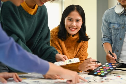 Smiling young creative woman discussing new app features with her colleagues during meeting at office.