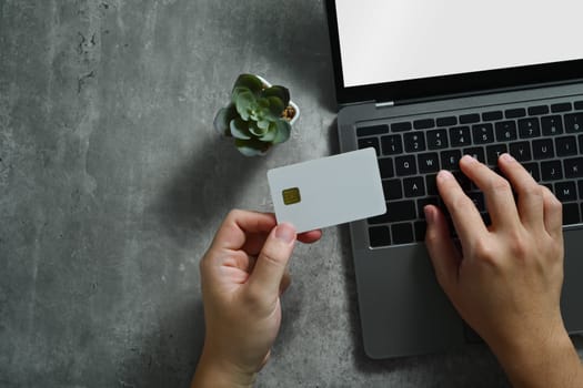 Unrecognizable man holding credit card, using laptop for online shopping or booking tickets.