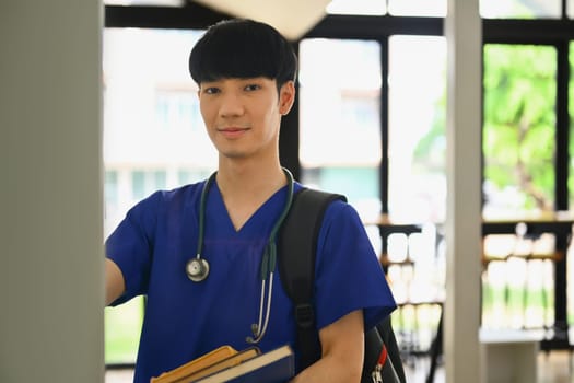 Photo of medical student standing at lockers in campus and smiling to camera. Medical internship concept.