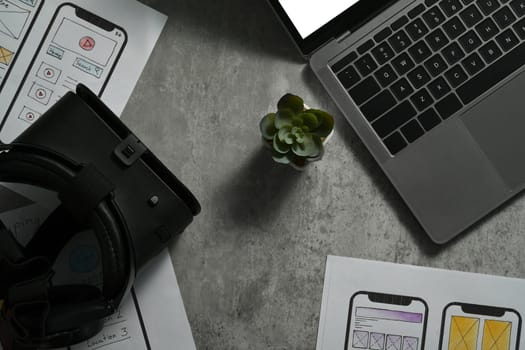 Virtual reality goggles, laptop and wireframe sketches of screens for mobile application on office desk.