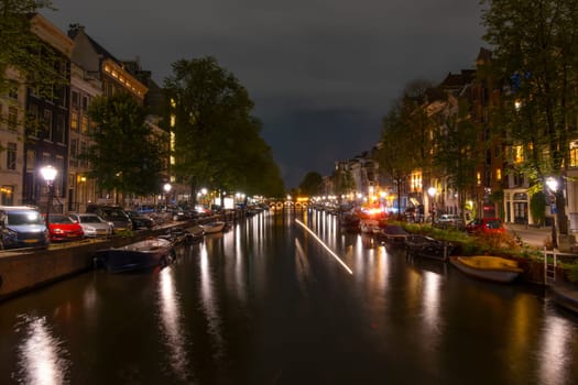 Netherlands. Summer night on the Amsterdam canal. Boats moored along the banks of the canal. Lanterns and parked cars on the embankments