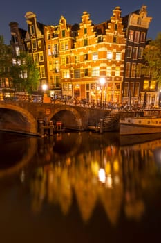 Netherlands. Night on the canal of Amsterdam. Dancing Dutch houses with lights. Bar with outdoor tables. Moored old boat