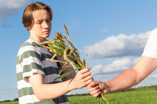 A young guy, a teenager with ears of ripe wheat in a farmer's field, against a blue sky. Grain for making bread. the concept of economic crisis and hunger