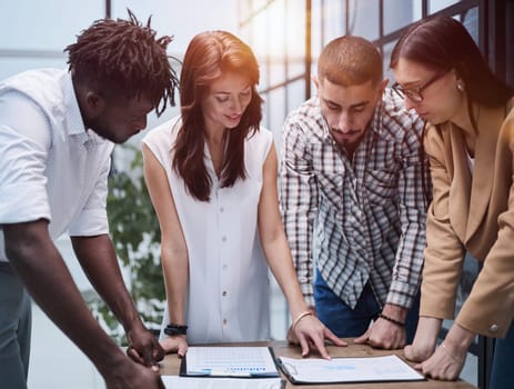 The concept of cooperation and brainstorming. Portrait of interracial friends gathered together, standing around a table in a classroom surrounded by books