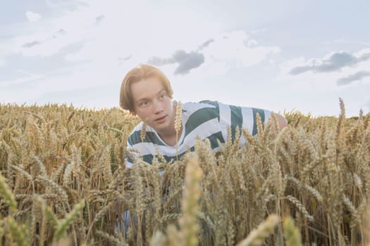 A young guy, a teenager with ears of ripe wheat in a farmer's field, against a blue sky. Grain for making bread. the concept of economic crisis and hunger