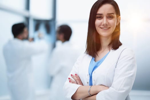 Young smiling woman-doctor is standing with arms crossed in a clinic office.