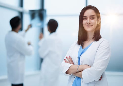 Young smiling woman-doctor is standing with arms crossed in a clinic office.