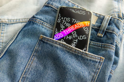 Tver, Russia - July 15, 2023, the threads logo on the smartphone screen lying on the jeans. The threads icon. The logo of the current application. Threads social network