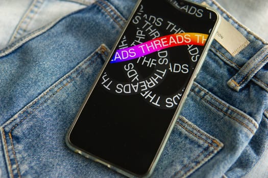 Tver, Russia - July 15, 2023, the threads logo on the smartphone screen lying on the jeans. The threads icon. The logo of the current application. Threads social network