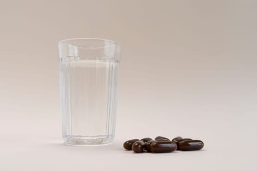 Selective Focus Lying Scattered Brown Sunflower Lecithin Softgel Pill Capsules And Glass Of Water On Beige Background. Dietary Supplements, Vitamins. Copy Space For Text. Healthy Lifestyle Horizontal.