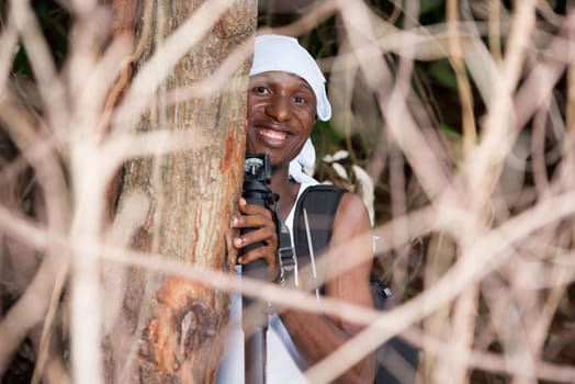 young man backpack with head tied up standing in bush looking at camera smiling.