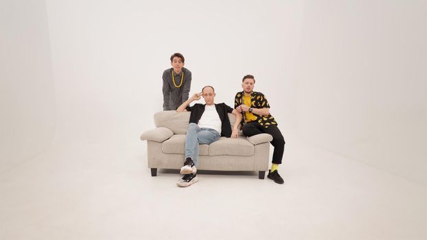 Three stylish young guys sitting on soft couch and talking on the camera. Group of friends are sitting on a soft couch and communicates isolated on white background. 4K footage.