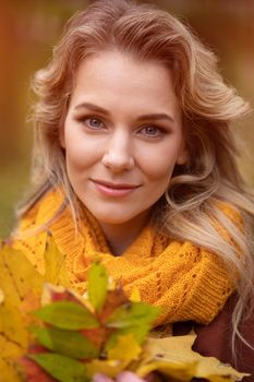 Young charming woman posing with fallen yellowed leaves for camera with walking around fall yellow garden or park. Beautiful smiling young woman in autumn leaves.