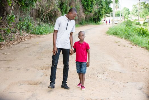 father walks with his young son in summer along the path in the park, the father holds the little son by the hand