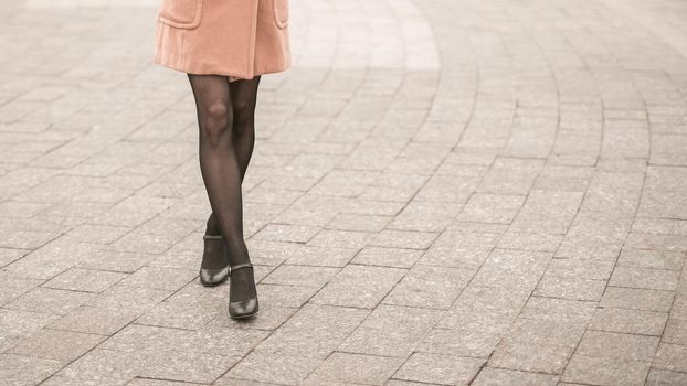 No face close up on legs making a cat walk of young woman on the street wearing autumn black shoes. Stylish young woman wearing autumn coat black nylon tights outdoors. Autumn accessories.