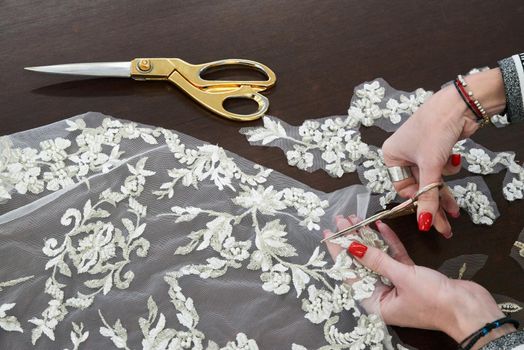 Dressmaker cutting lace fabric for wedding dress decoration