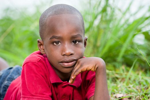 Portrait of cute happy boy lying in fresh green grass in sunny day, enjoying summer vacation.