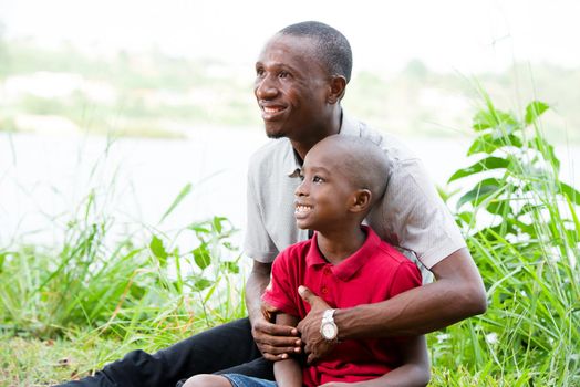 Portrait of father with his son sitting in grass, having fun in the park in summer happy family. little boy playing with dad outdoors