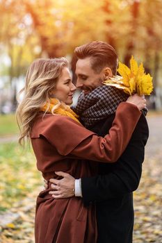 Half-length portrait of a kissing young couple. Husband and a wife hugged smile looking at each other in the autumn park. Outdoor shot of a young couple in love in a autumn park.