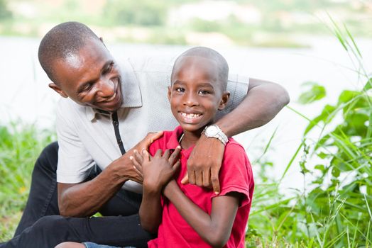 Portrait of father with his son sitting in grass, having fun in the park in summer happy family. little boy playing with dad outdoors