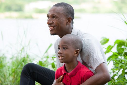 Portrait of father with his son sitting in grass, having fun in the park in summer happy family. little boy playing with dad outdoors