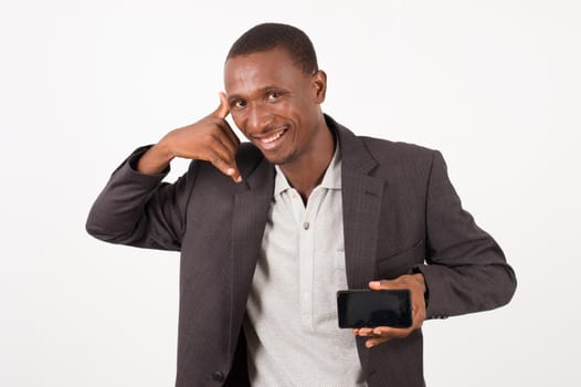 young man in a suit standing on a white background, mobile phone in hand giving a sign of communication with the other hand laughing.