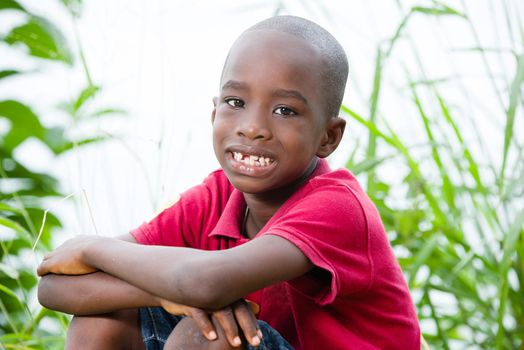 little boy smiles at the camera while sitting in a lush meadow on a beautiful summer afternoon