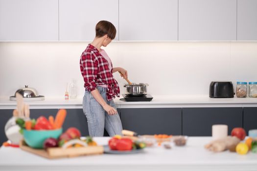 Pretty woman cooking dinner for big family stirring dish in the pot standing sideways to the camera. Healthy food living. Healthy lifestyle. Selective focus on vegetables.