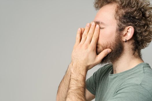 Has a headache young man touching his face. Handsome young man with curly hair in olive t-shirt isolated on white background.