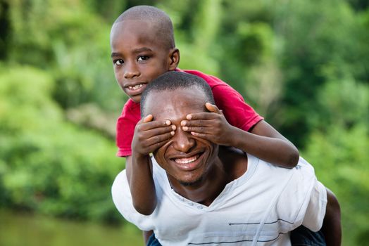 child sitting on his father's neck is holding his eyes closed.Happy young father and son having fun and enjoying the fresh air in nature.