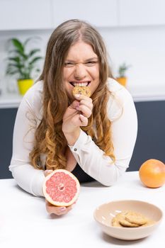 Happy curvy body young woman with long blond hair using blender at modern kitchen, blending fresh fruits for healthy smoothie. Dieting and nutrition concept.
